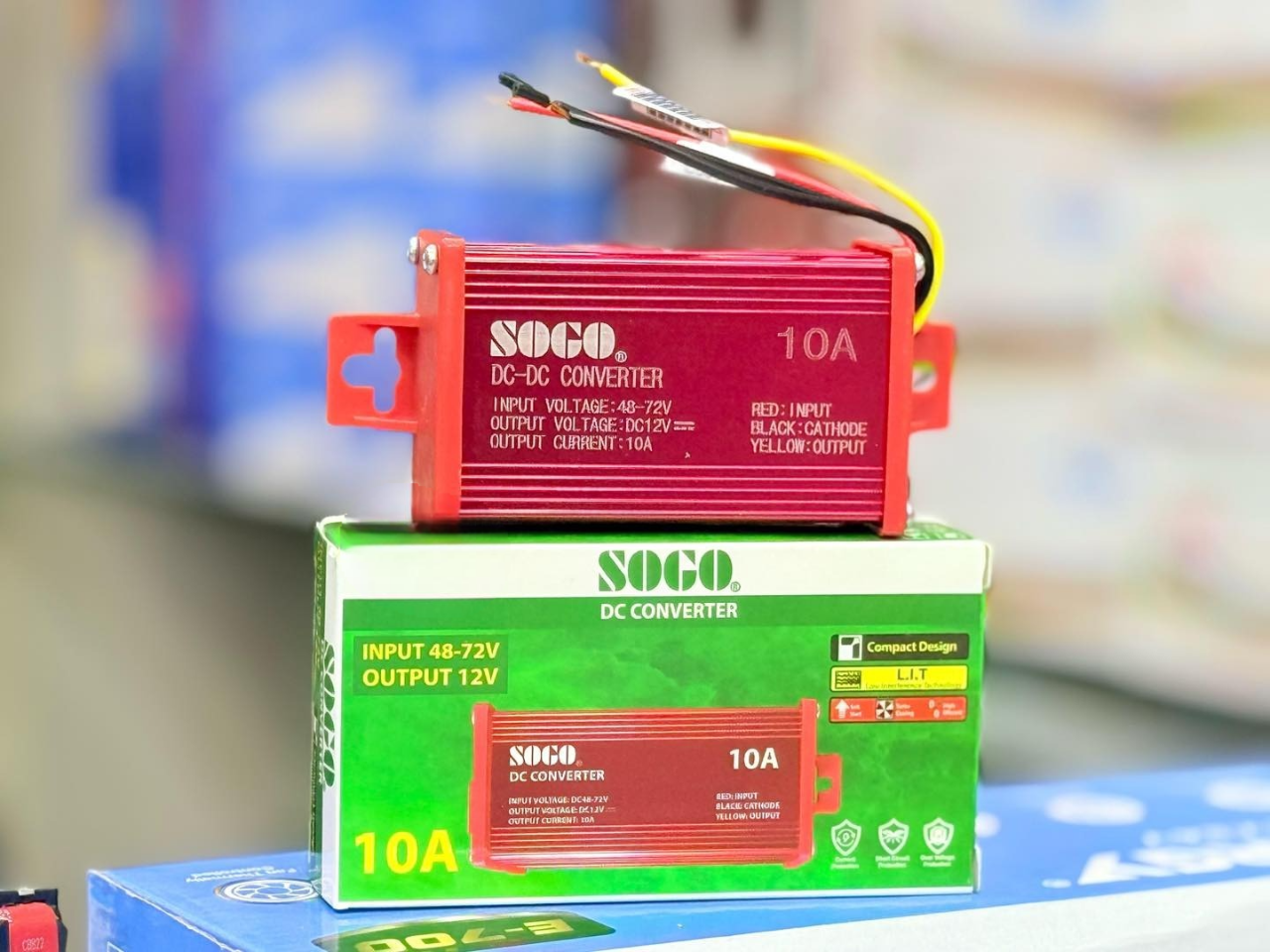 SOGO 10A DC Converter | 48-72V to 12V Step Down Voltage Regulator - a red rectangular voltage regulator with three wires sitting atop its green and white product packaging box.