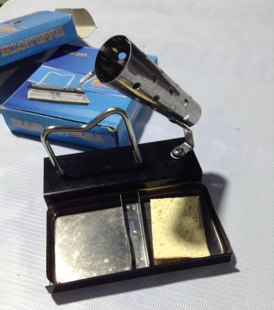 Soldering Iron Stand - a black metal base, a coiled wire holder, a cleaning sponge, and its blue branded packaging box in the background.