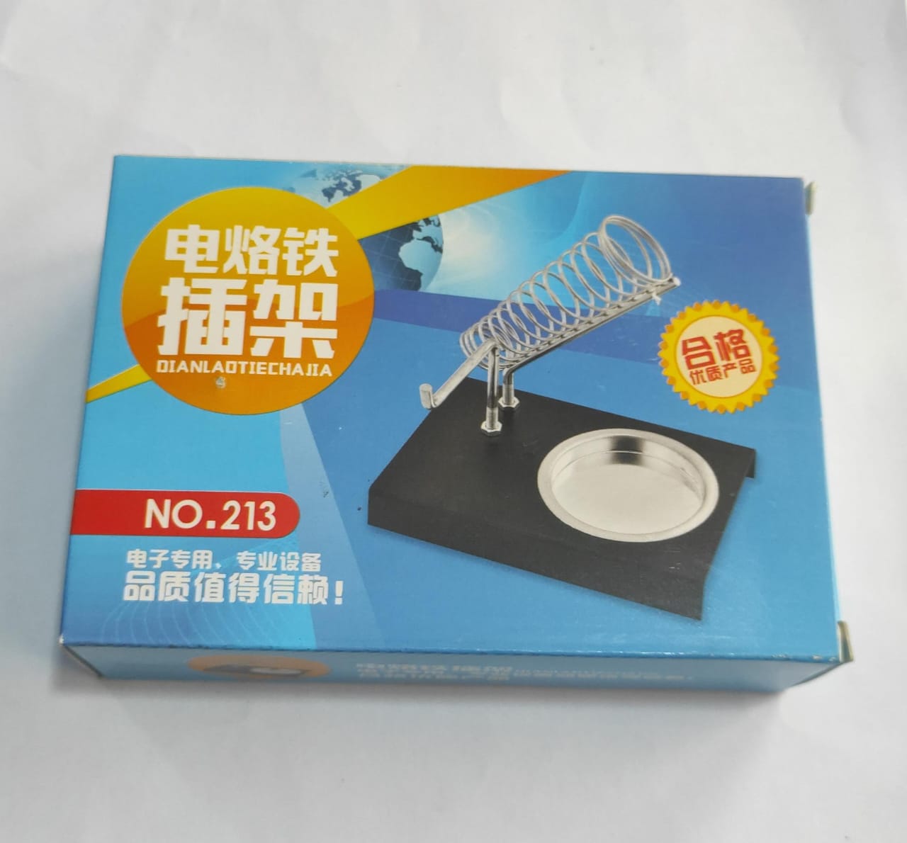 Soldering Iron Stand Holder - shown in its blue retail packaging box, featuring a black base, a metal coil holder, and a circular tray.