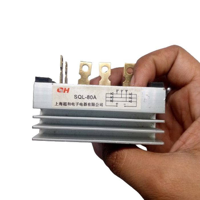 SQL-80A THREE PHASE BRIDGE - a silver metallic bridge rectifier with cooling fins and five top-mounted electrical terminals, held by a hand.