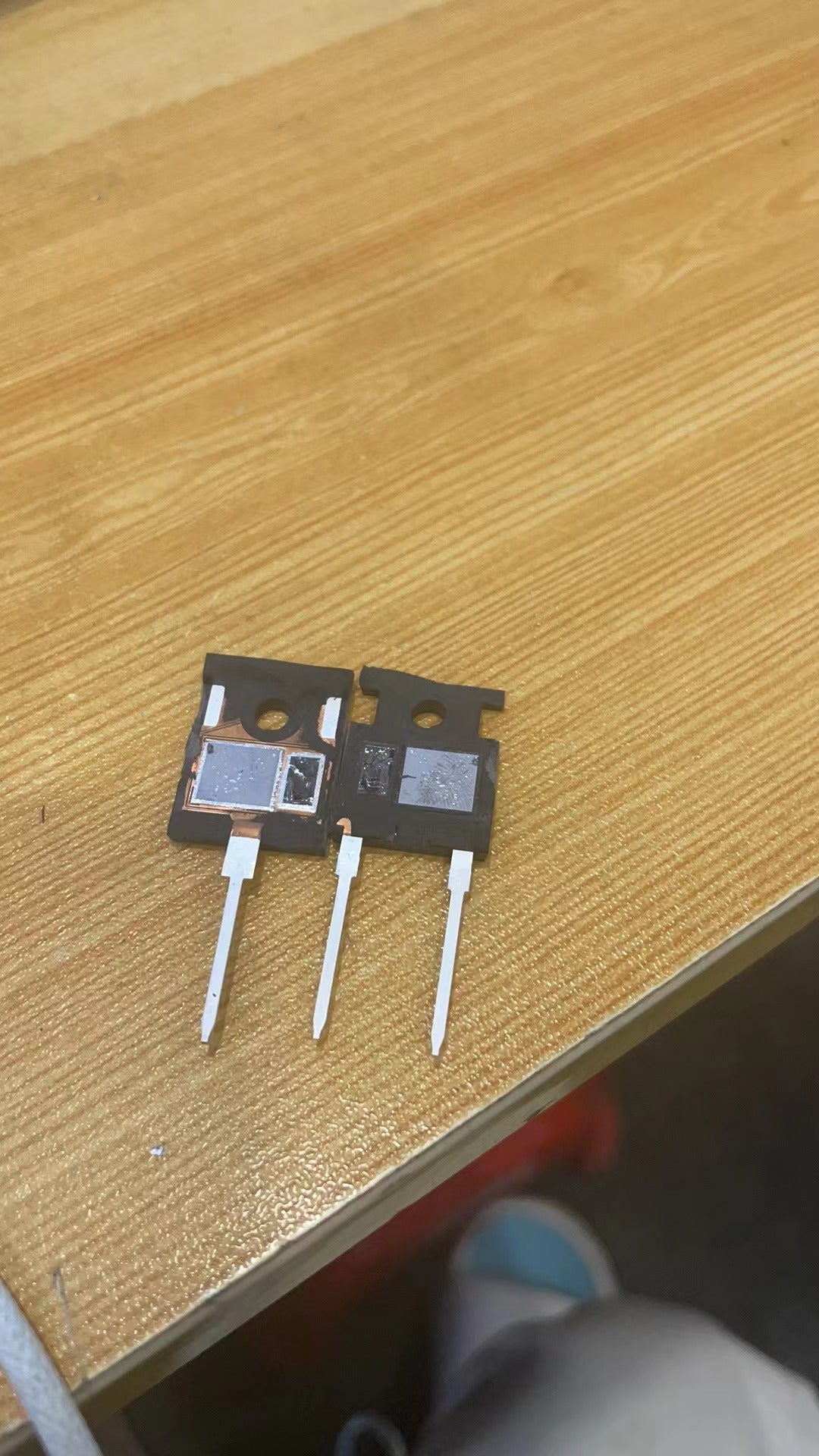 SRE100N65 IGBT - High-Performance Transistor for Power Electronics - two black, three-pin power transistors with their internal semiconductor dies exposed, resting on a wooden surface.