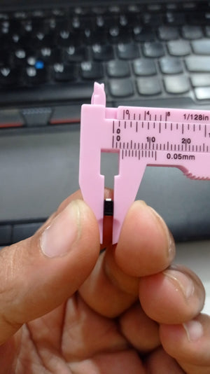 SS56 SMD 5A 60V DO-214AA Schottky Diode - a small black electronic component held in a pink plastic vernier caliper for a size measurement close-up.
