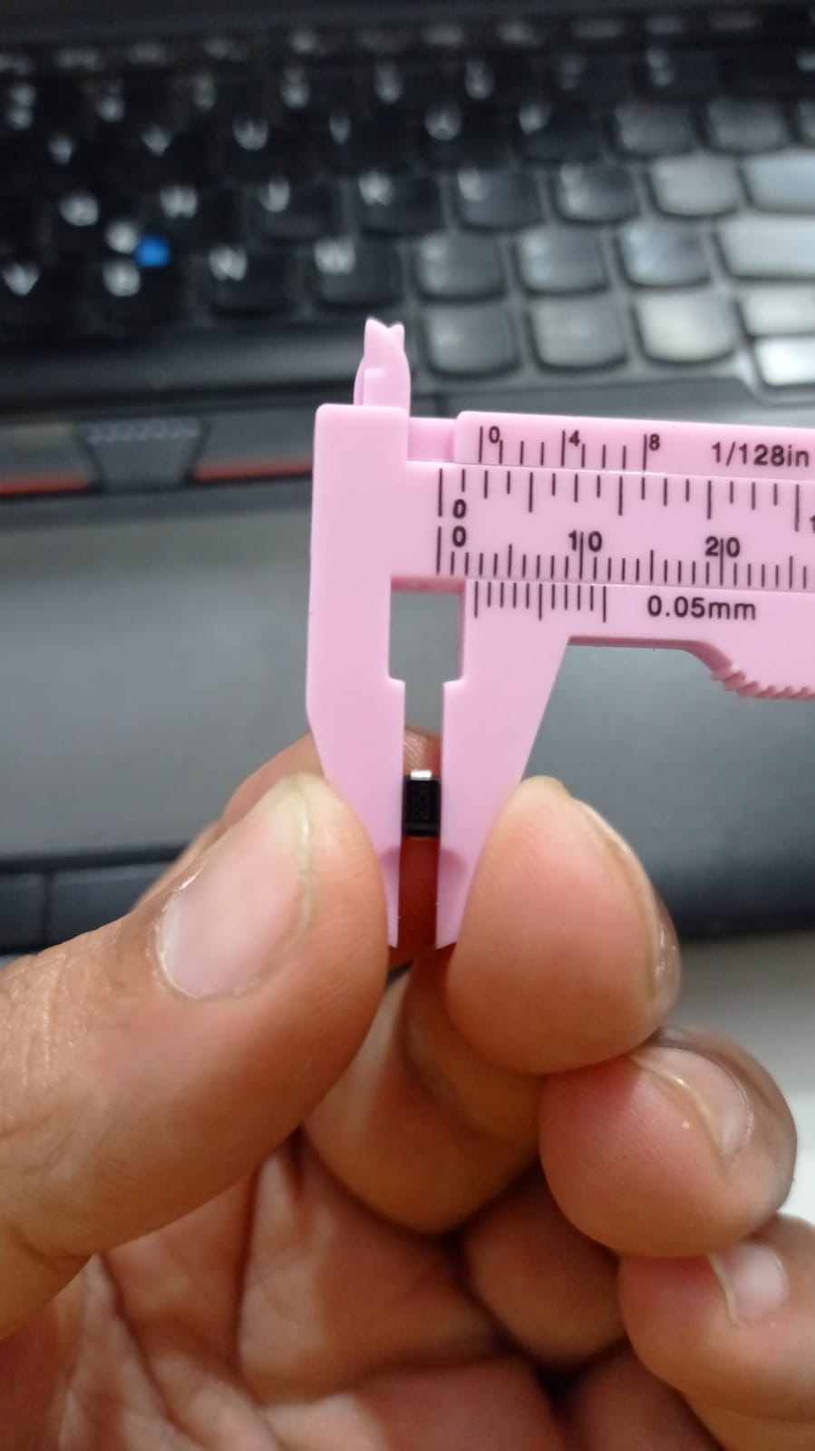 SS56 SMD 5A 60V DO-214AA Schottky Diode - a small black electronic component held in a pink plastic vernier caliper for a size measurement close-up.