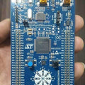 Stm Discovery Kit STM32F3 STM32F303VC With Programming Cable - a blue rectangular development board held in a hand, featuring two USB ports, a central microcontroller, buttons, and LEDs.
