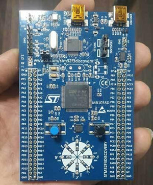 Stm Discovery Kit STM32F3 STM32F303VC With Programming Cable - a blue rectangular development board held in a hand, featuring two USB ports, a central microcontroller, buttons, and LEDs.