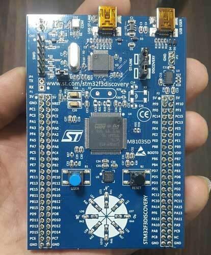 Stm Discovery Kit STM32F3 STM32F303VC With Programming Cable - a blue rectangular development board held in a hand, featuring two USB ports, a central microcontroller, buttons, and LEDs.