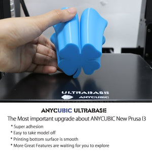 Stock Lot Assembled Anycubic Full Metal I3 Mega 3D Printer with Ultrabase Heatbed and 3.5 Inch Touch Screen - a hand holding a blue, clover-shaped 3D printed object above the black Ultrabase heatbed.
