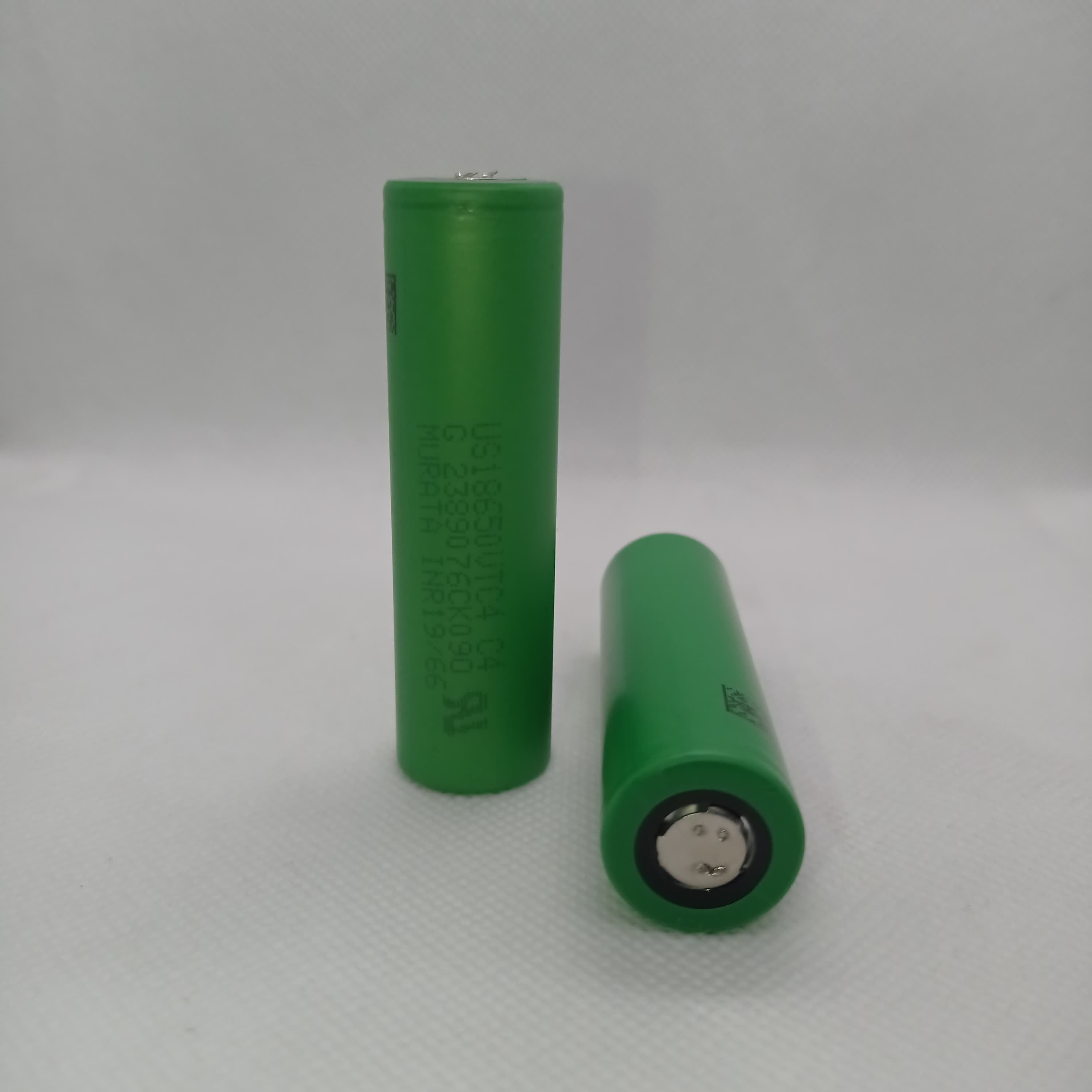 Stock Lot US18650UTC4 3.7V 2000mA 18650 Li-ion Rechargeable Battery – High-Capacity Power Cell for Flashlights, Laptops, and Power Tool - two green cylindrical cells shown with one standing upright and one lying horizontally on a white surface.