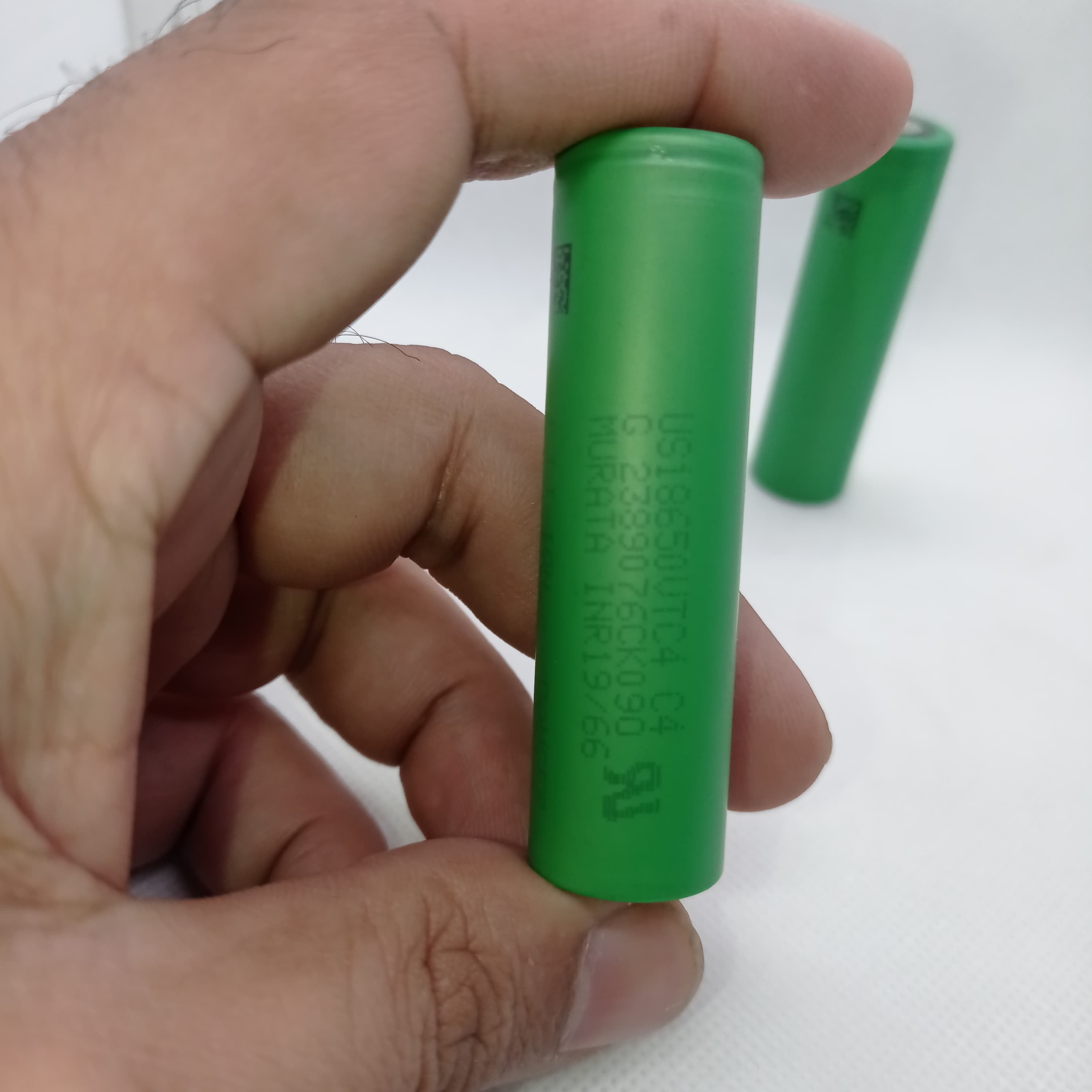 Stock Lot US18650UTC4 3.7V 2000mA 18650 Li-ion Rechargeable Battery – High-Capacity Power Cell for Flashlights, Laptops, and Power Tool - the green cylindrical casing with printed specifications and a second battery in the background.