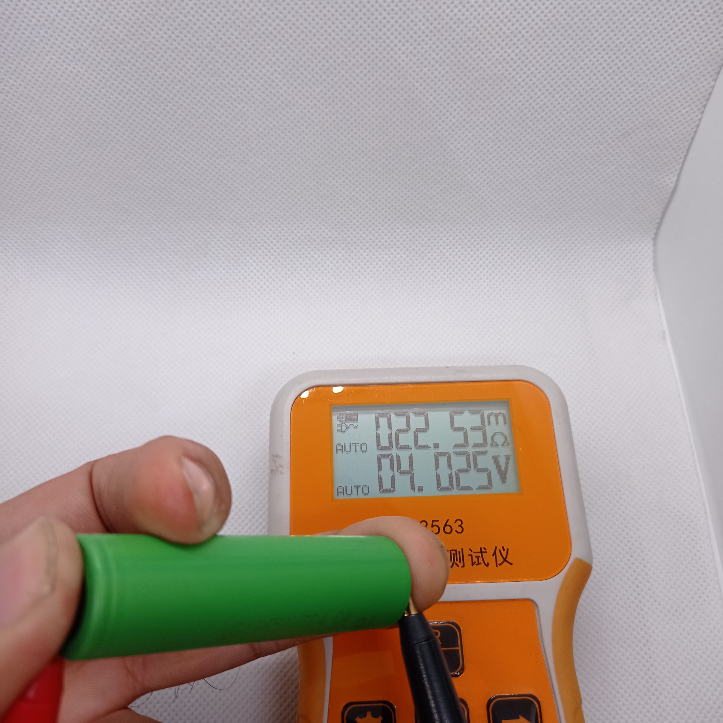 Stock Lot US18650UTC4 3.7V 2000mA 18650 Li-ion Rechargeable Battery – High-Capacity Power Cell for Flashlights, Laptops, and Power Tool - held against a battery tester showing 22.53mΩ internal resistance and 4.025V on the digital display.