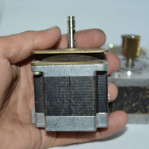 Stock Lot Used Bipolar NEMA 23 Stepper Motor Lot - a close-up shot of a silver and black square motor held in a hand with a metal shaft extending from the top.