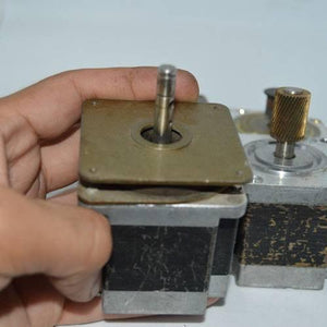 Stock Lot Used Bipolar NEMA 23 Stepper Motor Lot - a close-up of two metallic stepper motors with shafts held by a hand.