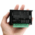 TB6600 Stepper Motor Driver - held in a hand, showing the black rectangular housing with a green terminal block and a printed configuration table.