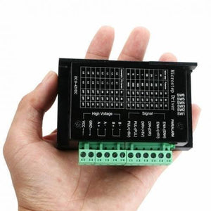 TB6600 Stepper Motor Driver - held in a hand, showing the black rectangular housing with a green terminal block and a printed configuration table.