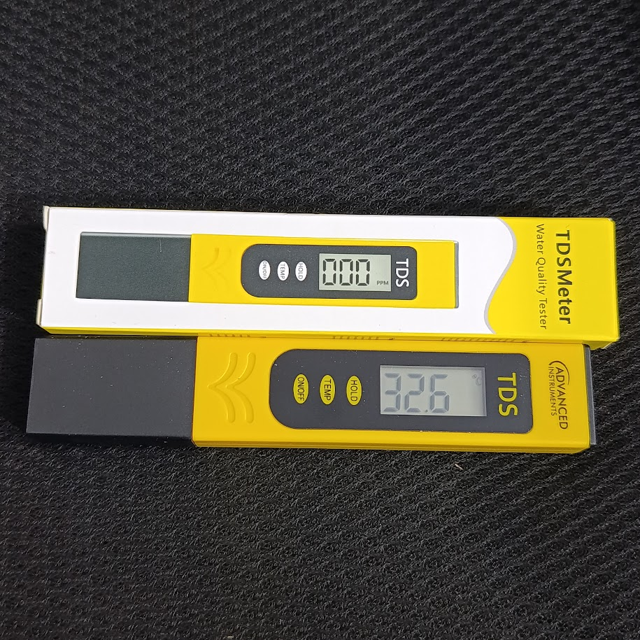 TDS Meter - Water Quality Tester - shown with one unit in its yellow packaging and another unit below it displaying 32.6 with buttons for on/off, temp, hold.