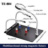 TE-804 Soldering Third Hand Magnetic Universal PCB Motherboard Fixture With Magnifier - a black magnetic workbench with two flexible arms, alligator clips, and a magnifying glass on a universal tube.