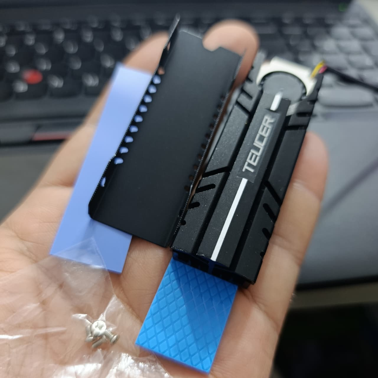TEUCER M.2 SSD Heatsink NVME 2280 - Aluminum Cooling Radiator for Desktop PC & PS5 - the black aluminum heatsink, a base plate, two blue thermal pads, and small mounting screws in a plastic bag.