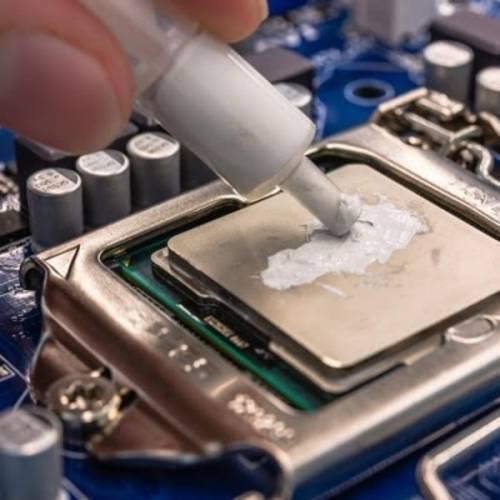 Thermal Compound Grease Gel Heat Sink Paste - white syringe being applied to a silver computer processor on a blue motherboard.