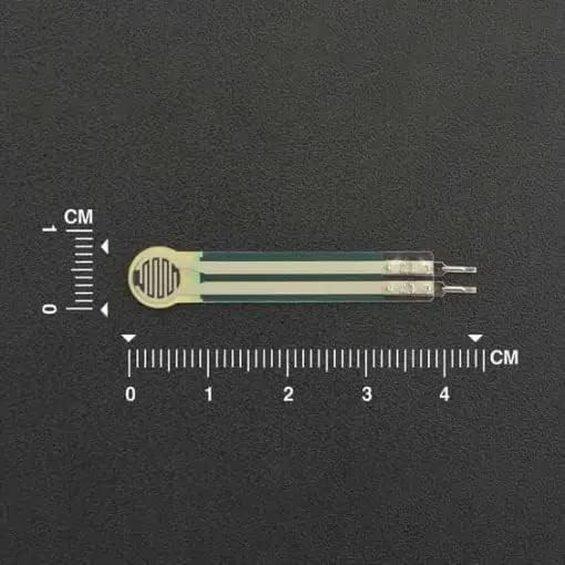 Thin Film Pressure Sensor FSR RP-C7.6-LT-LF2 Flexible High Sensitivity 30G to 8KG - shown as a flat, flexible, light-colored sensor strip with two metal pins, positioned against a ruler scale.