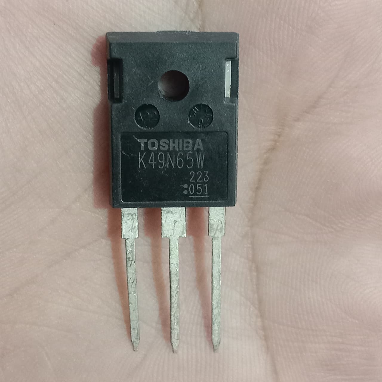 Toshiba K49N65W N-Channel Power MOSFET - a close-up view of a black, three-pin electronic component held against a palm, showing printed text on its face.
