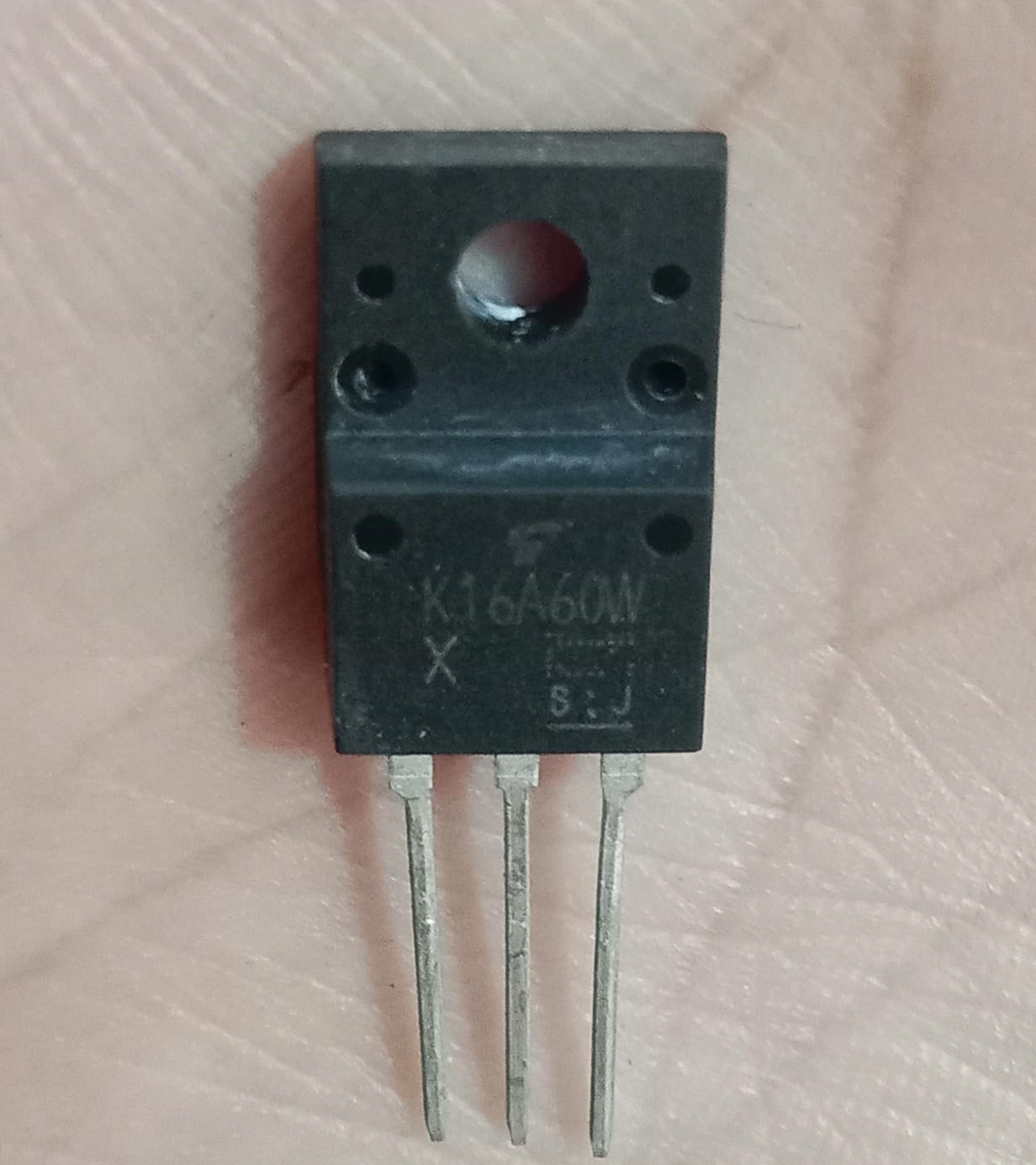 Toshiba TK16A60W 600V 15.8A N-Channel Power MOSFET (TO-220SIS) USED - a black, three-pin electronic component with a mounting hole, shown in a close-up view against a skin-toned background.