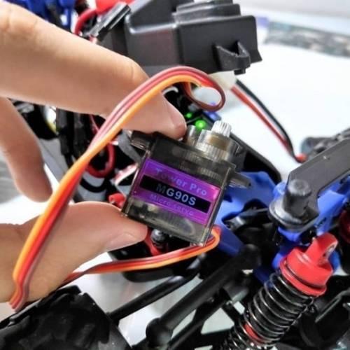 Towerpro MG90S Mini Digital 180 Degree Servo Motor 2.2kg 0.08sec 13G - a small black motor with a purple label being held by a hand over a remote-controlled car chassis.