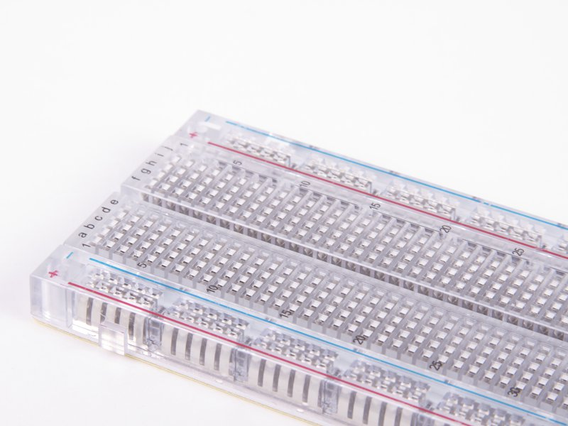 Transparent Clear Breadboard 830 Tie-Points with 4 Sets of Power Rails - a close-up angled view of the clear plastic grid and labeled terminals.