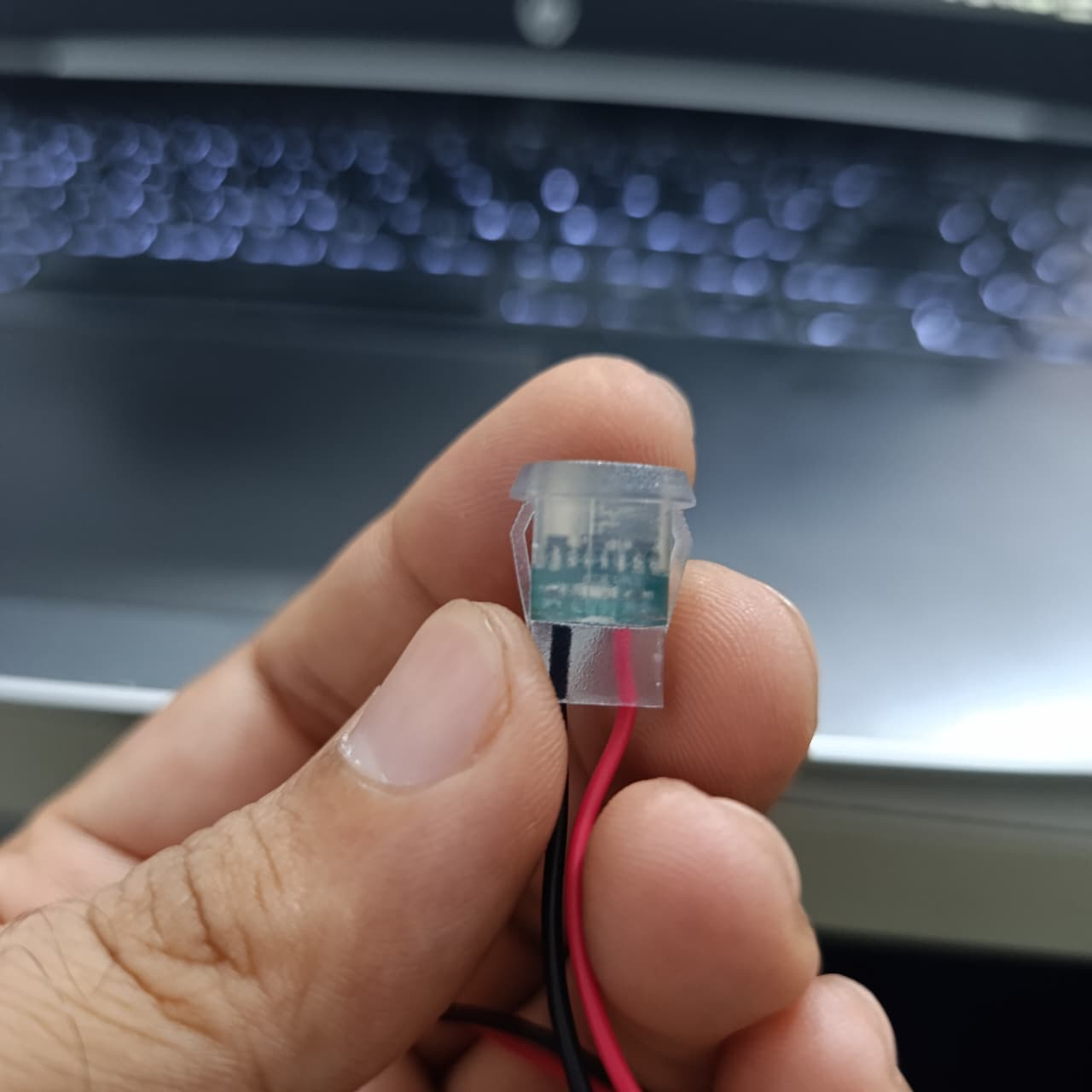 Type-C 2P Round Transparent Green Light USB Female Port – LED Plug-in Type - close-up of the component held in fingers with red and black wires attached to the base.