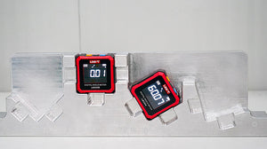 UNI-T LM320B Digital Laser Angle Meter – 4×90° Inclinometer, ±0.2° Accuracy, 0.01° Resolution, Two-Side Lasers, Four-Side Magnetic Base, EBTN Display, Type-C Rechargeable - two red and black square meters on a metal jig, displaying 0.01 and 60.07 on their backlit screens.