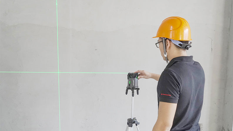 UNI-T LM555LD 4D Green Laser Level – 4V1H + Plumb Point, ±2 mm/10 m, Self-Leveling, 130° Lines, IP54, Rechargeable - projecting green crosshair lines onto a wall while being adjusted by a worker in a hard hat.