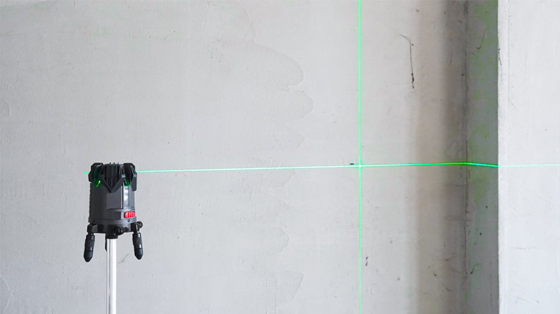 UNI-T LM555LD 4D Green Laser Level – 4V1H + Plumb Point, ±2 mm/10 m, Self-Leveling, 130° Lines, IP54, Rechargeable - projecting horizontal and vertical green laser lines onto a plain wall with a visible red power button.