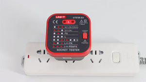UNI-T UT07A-EU Socket Tester for EU Schuko Outlets – Mains Power Socket Wiring Fault Checker with Earth (PE), Live, Neutral & Reverse Polarity Detection, 230V 50/60Hz - UNI-T UT07B-EU socket tester plugged into a white power strip, showing red LED indicator lights on its face and a red leakage test button on the side.