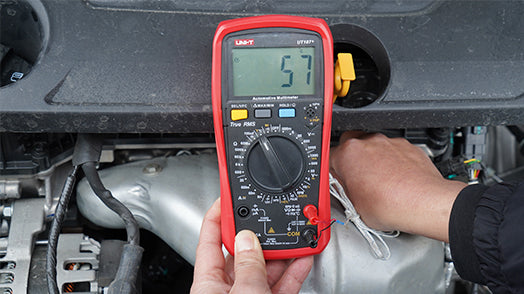 UNI-T UT107+ True RMS Automotive Multimeter – 6000 Count, RPM, Dwell Angle, Pulse Width, Battery Test, Temperature, 1000V AC/DC, VFC, CAT III 600V - a red handheld device with a central dial and digital screen displaying 57, held against a car engine.