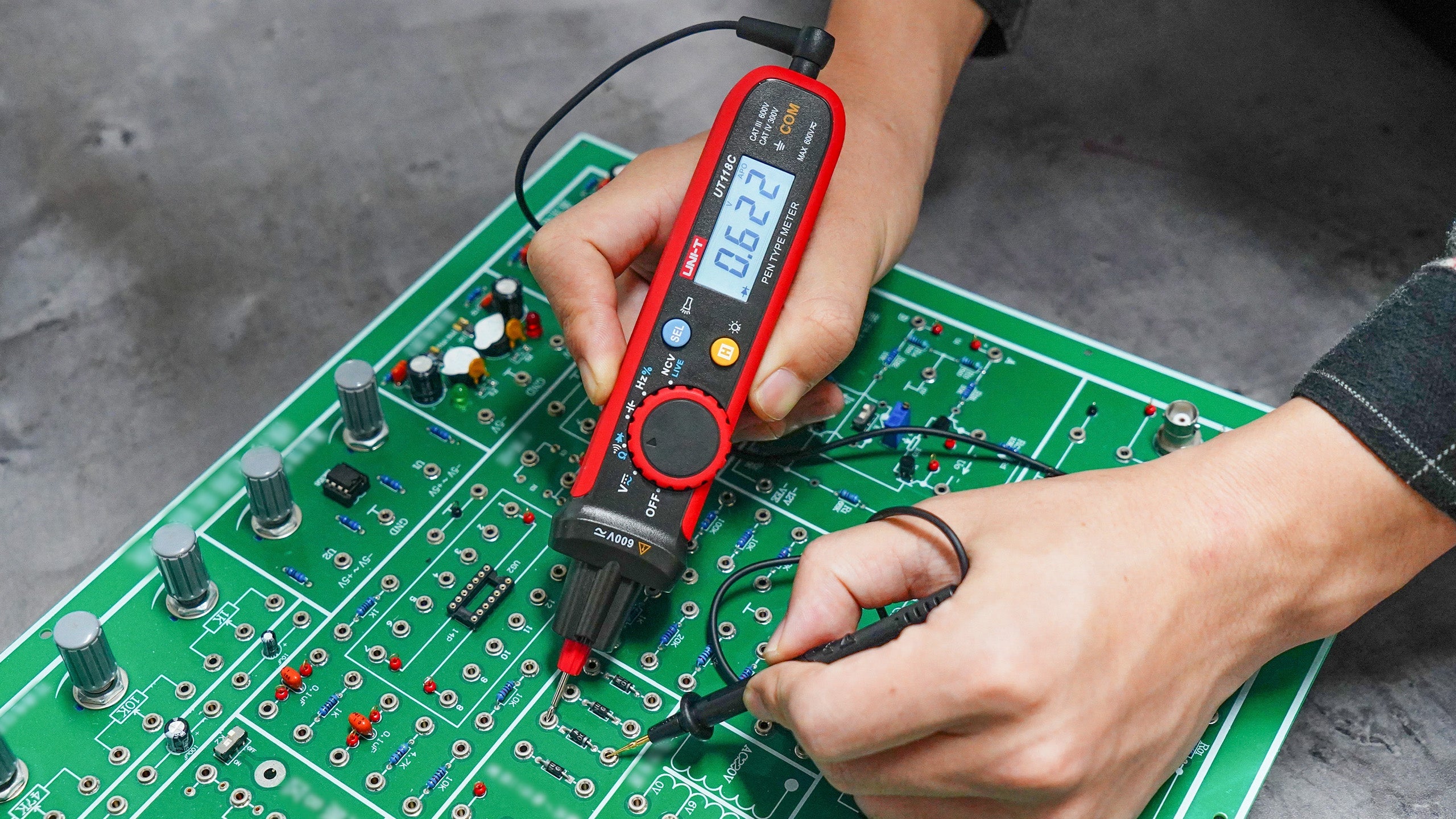 UNI-T UT118C True RMS Pen Type Digital Multimeter – AC/DC 600V, Resistance, Capacitance, NCV, Gold-Plated Tips, CAT III 600V / CAT IV 300V - held by hands testing a green circuit board, with the digital display showing 0.622.
