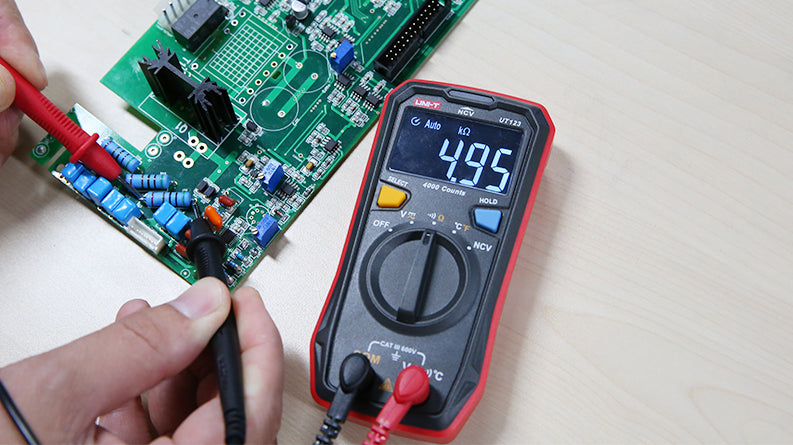 UNI-T UT123 Pocket Residential Digital Multimeter – EBTN Display, AC/DC Voltage, Resistance, Temperature, NCV, Diode & Continuity, One-Hand Design - a 4.95 kΩ reading on its EBTN display while probes test a green circuit board on a light-coloured surface.