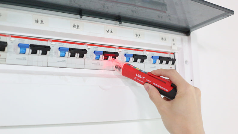 UNI-T UT12D Non-Contact AC Voltage Detector Pen – 24V to 1000V NCV Tester with LED Flashlight, Buzzer & LED Alert, Dual High/Low Sensitivity, Auto Power-Off, 1m Drop-Proof - a red handheld device with a glowing red tip, being used to test an electrical circuit breaker panel.