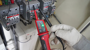 UNI-T UT15C Waterproof Voltage & Continuity Tester Pen with LCD Display – AC/DC up to 690V, Three-Phase Rotation, IP65, Digital Readout & Single-Probe Live Wire Detection - and black handheld device with a digital display showing 389, being used to test electrical terminals by a gloved hand.