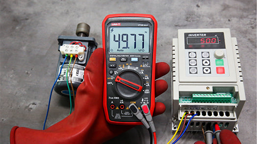 UNI-T UT18B MAX True RMS Digital Multimeter – 6000 Count, 1000V AC/DC, VFD, Temperature, LED Test, Capacitance, Frequency, EMI Protection with Gold-Plated Leads - held in a gloved hand, showing a 49.77 Hz reading on its display, next to a motor and an inverter.