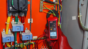 UNI-T UT251C+ AC Leakage Current Clamp Meter – 1µA Resolution, 3mA to 60A, 40mm Jaw, Harmonic Test, LPF, Bluetooth, Dual Display, CAT III 600V - held by a gloved hand, measuring wires with its jaw and showing 24.99 on the digital display.