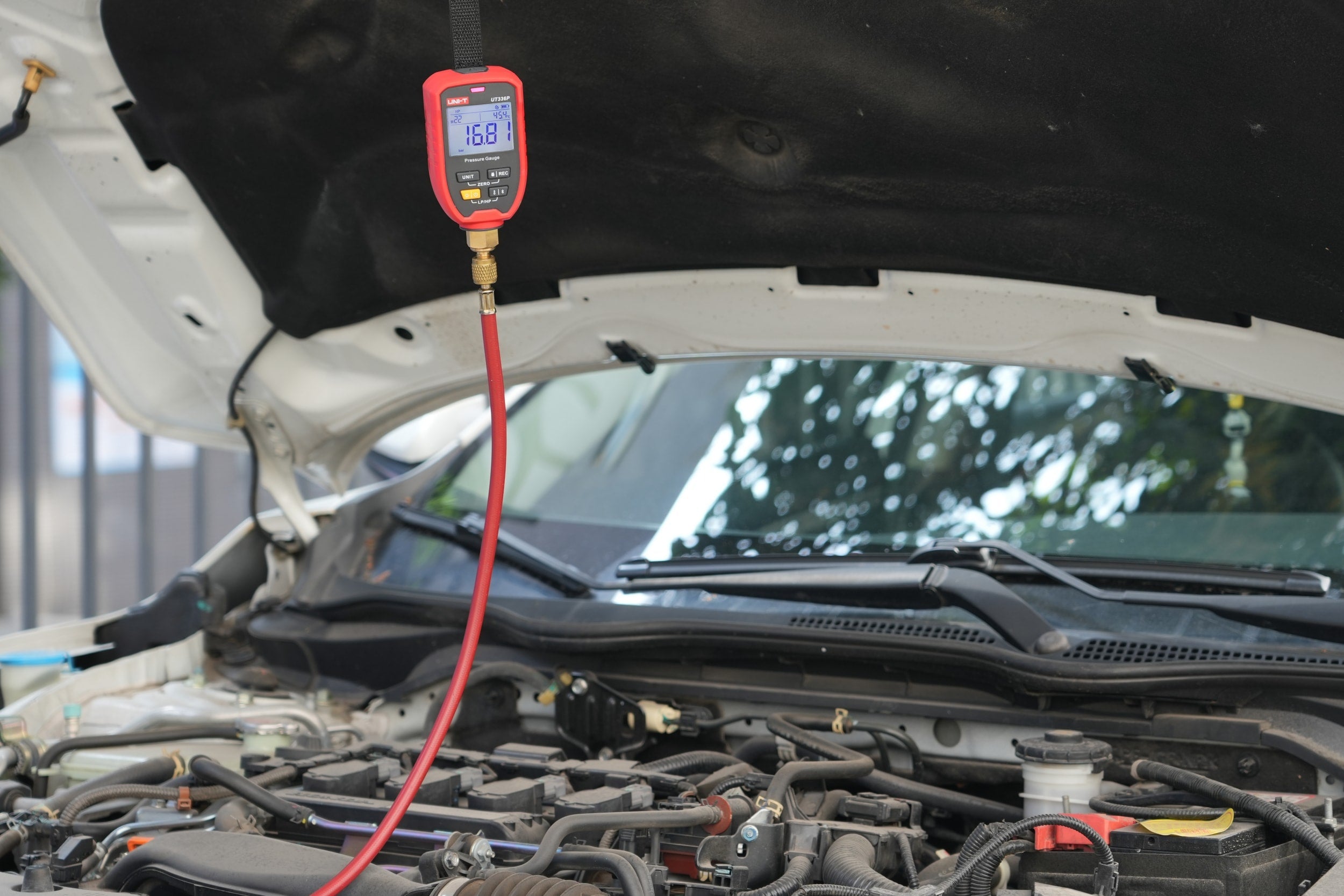 UNI-T UT336P KIT Wireless Digital Pressure Gauge with Temperature Clamp – -1 to 60 bar, HVAC Refrigerant Manifold, 94 Refrigerants, App Connected - red casing, digital display showing 16.8, and a red hose connected to a car engine bay.