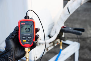 UNI-T UT336P KIT Wireless Digital Pressure Gauge with Temperature Clamp – -1 to 60 bar, HVAC Refrigerant Manifold, 94 Refrigerants, App Connected - held in a gloved hand, showing a red casing, buttons, a brass connector, and a screen reading 5.01 bar for R22.