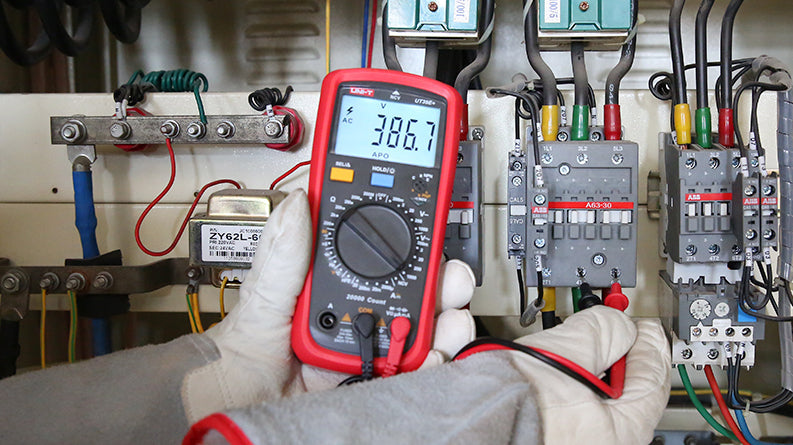 UNI-T UT39A+ Digital Multimeter – 4000 Count, AC/DC 1000V, 10A, Capacitance, hFE, NCV, Diode & Continuity, CAT II 1000V / CAT III 600V - held by gloved hands, displaying 386.7V AC while connected to electrical control panel terminals with red and black probes.