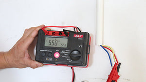 UNI-T UT502A Insulation Resistance Tester – Digital Megohmmeter, 500V/1000V/2500V - display reading 5.50 GΩ and 523V, with a hand holding the device connected to colored wires.