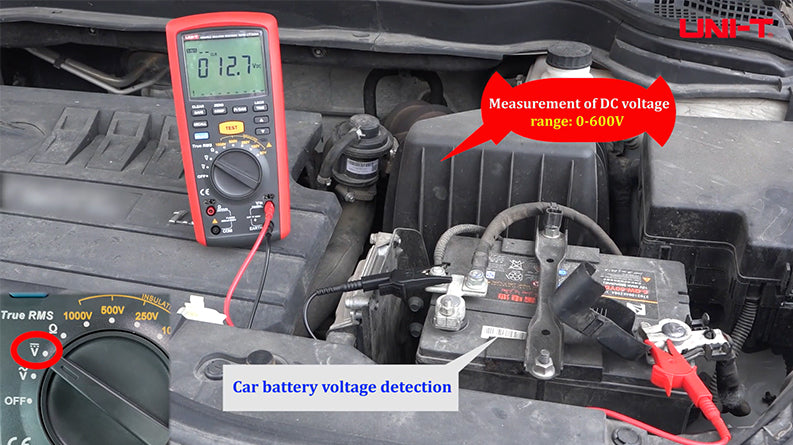 UNI-T UT505B Insulation Resistance Tester – Digital Megohmmeter, 100V/250V/500V/1000V - a red and black handheld device with a digital display showing 12.7, measuring a car battery's DC voltage.