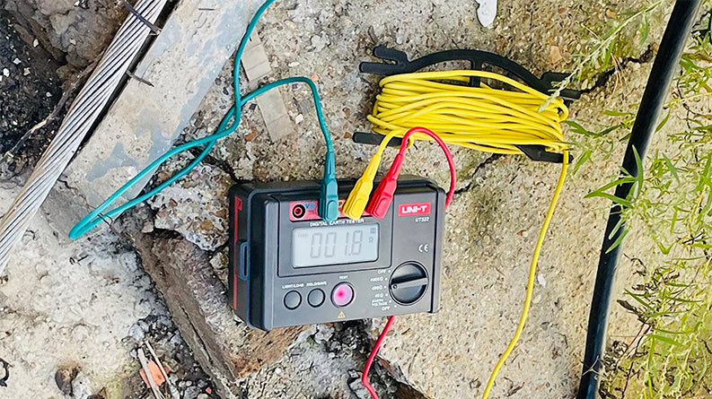 UNI-T UT522 Earth Resistance Tester – Digital Earth / Ground Resistance Meter - display reading 001.8, connected to three colored test leads and a yellow cable reel on ground.