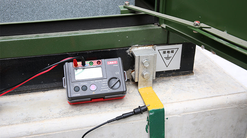 UNI-T UT526 Multifunction Electrical Tester – Multifunction Installation Tester, 250V/500V/1000V - with a grey and red body, a digital display, a rotary dial, and test leads connected to a metal grounding terminal.