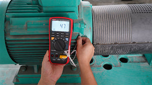 UNI-T UT533 Insulation Multimeter – Insulation Tester + Digital Multimeter - held against a green motor, showing a red and black casing, a digital display reading 47, and connected test leads.