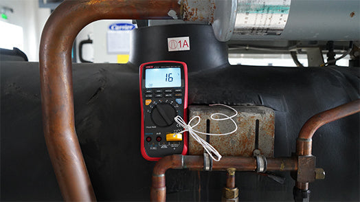UNI-T UT533 Insulation Multimeter – Insulation Tester + Digital Multimeter - a red and black handheld device with a digital display showing 16, connected to a white probe on industrial piping.