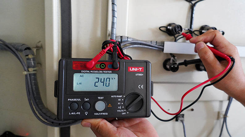 UNI-T UT582+ RCD / ELCB Tester – Digital RCD / ELCB Trip Tester - with red and black test leads connected, showing a 240V reading on the digital display and a rotary dial.