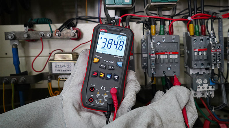 UNI-T UT60S True RMS Digital Multimeter – 9999 Count, AC/DC 1000V, 10A, Capacitance, Frequency, Temperature, NCV, 3-Color LED Alert, CAT III 600V - held in gloved hands, displaying 384.8V AC and 50.03Hz, with red and black probes connected to the bottom ports.
